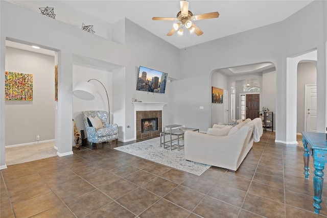 tiled living room with a tiled fireplace, a high ceiling, and ceiling fan