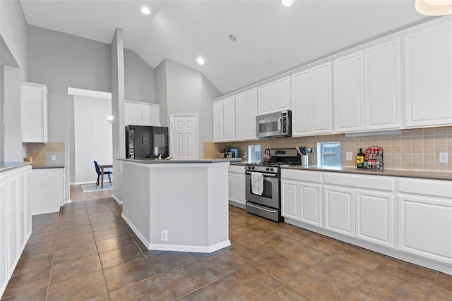 kitchen with appliances with stainless steel finishes, white cabinetry, lofted ceiling, dark tile patterned flooring, and decorative backsplash