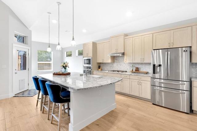 kitchen featuring appliances with stainless steel finishes, a kitchen island with sink, light stone countertops, decorative backsplash, and decorative light fixtures