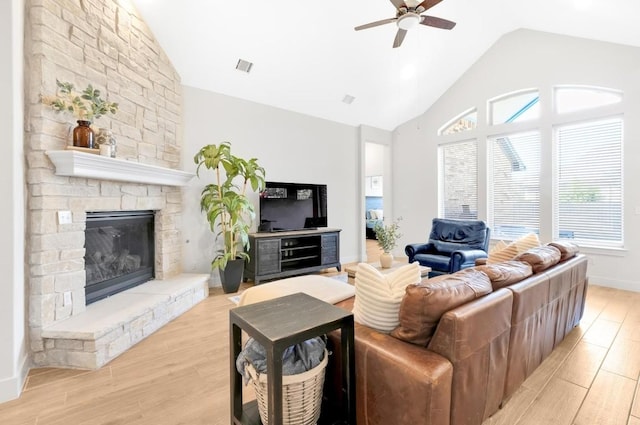 living room featuring a stone fireplace, high vaulted ceiling, ceiling fan, and light hardwood / wood-style flooring