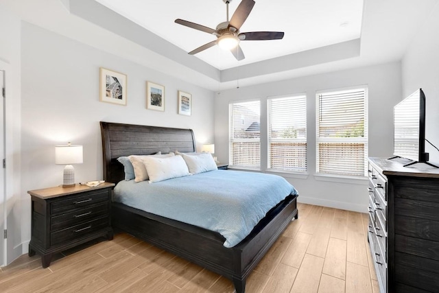 bedroom featuring ceiling fan, a raised ceiling, and light hardwood / wood-style floors