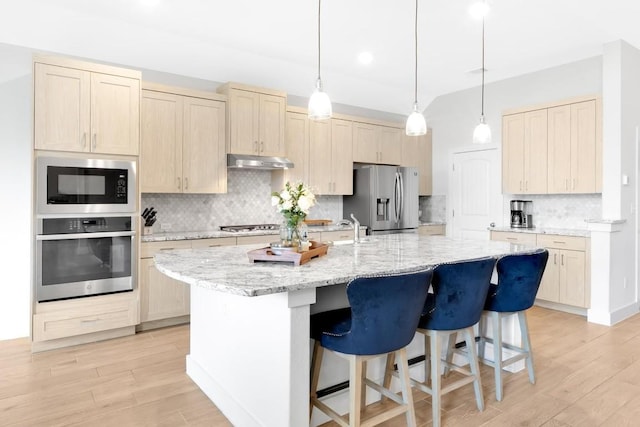 kitchen featuring stainless steel appliances, a center island with sink, light stone counters, and light hardwood / wood-style flooring