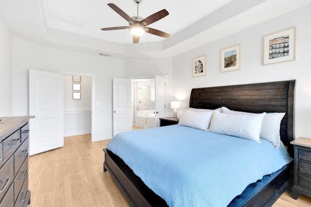 bedroom featuring connected bathroom, a tray ceiling, light hardwood / wood-style flooring, and ceiling fan