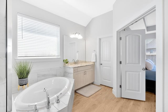 bathroom with wood-type flooring, lofted ceiling, tiled bath, and vanity