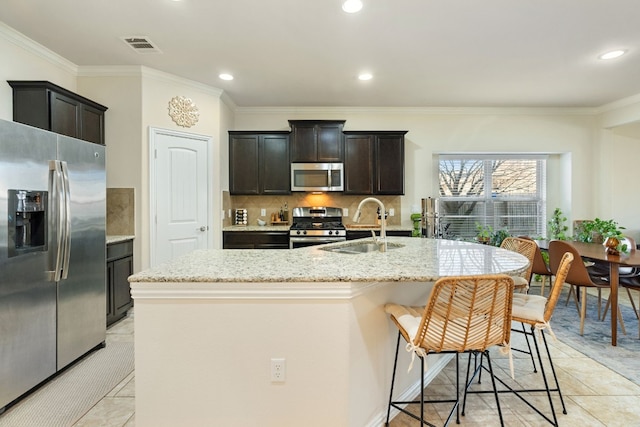 kitchen featuring stainless steel appliances, sink, a kitchen island with sink, and light stone counters