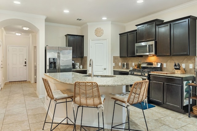 kitchen featuring sink, crown molding, appliances with stainless steel finishes, an island with sink, and light stone countertops