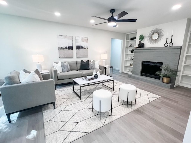 living room with a brick fireplace, built in features, ceiling fan, and light wood-type flooring