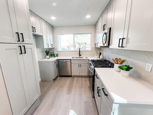 kitchen featuring stainless steel appliances, sink, light hardwood / wood-style flooring, and backsplash