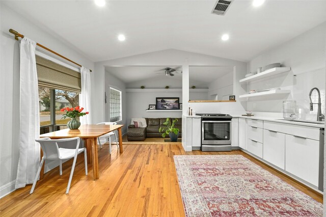 kitchen with lofted ceiling, sink, white cabinetry, stainless steel range, and a fireplace