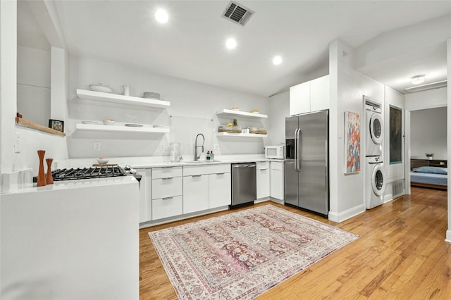 kitchen with sink, white cabinets, stacked washer and dryer, and stainless steel appliances