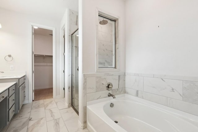 full bathroom featuring marble finish floor, a garden tub, a spacious closet, a shower stall, and vanity