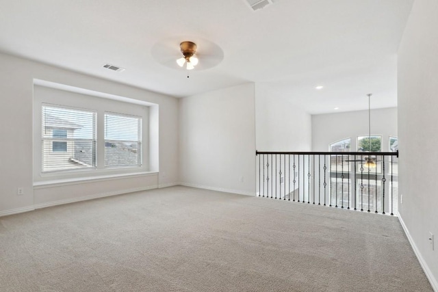 carpeted empty room featuring a ceiling fan, baseboards, visible vents, and a wealth of natural light