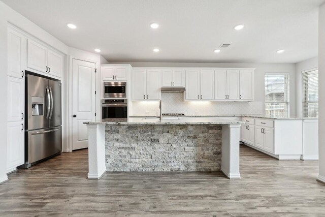 kitchen with stainless steel appliances, a center island with sink, and white cabinets