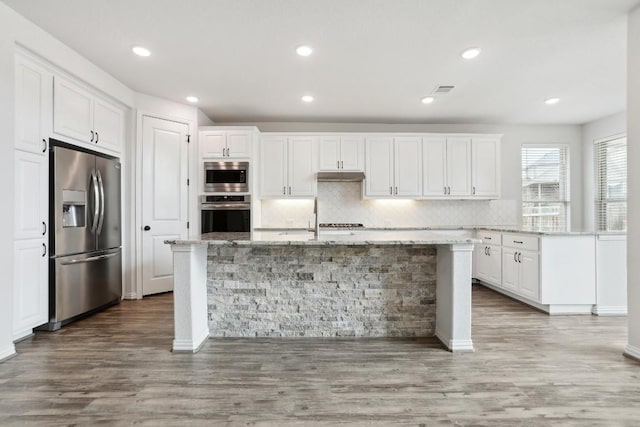 kitchen with wood finished floors, white cabinetry, appliances with stainless steel finishes, decorative backsplash, and a center island with sink