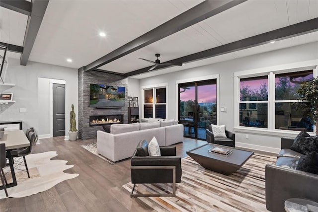 living room featuring ceiling fan, a large fireplace, beam ceiling, and light hardwood / wood-style floors