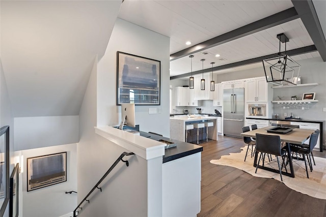 kitchen with pendant lighting, dark wood-type flooring, beam ceiling, stainless steel appliances, and white cabinets