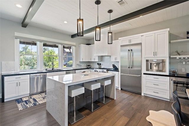 kitchen featuring a kitchen island, appliances with stainless steel finishes, pendant lighting, white cabinetry, and sink