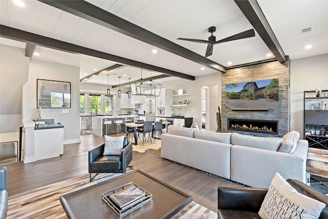 living room with beamed ceiling, wood-type flooring, ceiling fan, and a fireplace