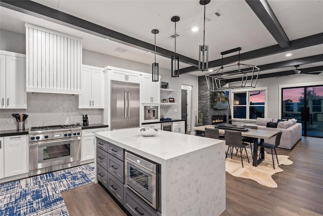 kitchen with pendant lighting, built in appliances, a kitchen island, and white cabinets