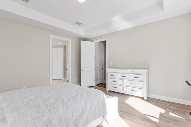 bedroom with light hardwood / wood-style flooring and a raised ceiling