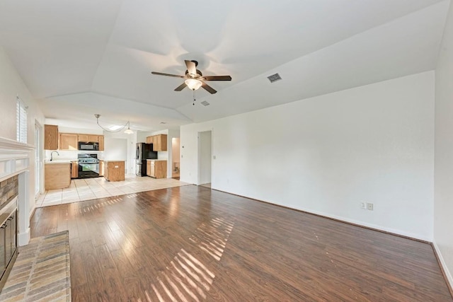 unfurnished living room with vaulted ceiling, sink, ceiling fan, light hardwood / wood-style floors, and a brick fireplace