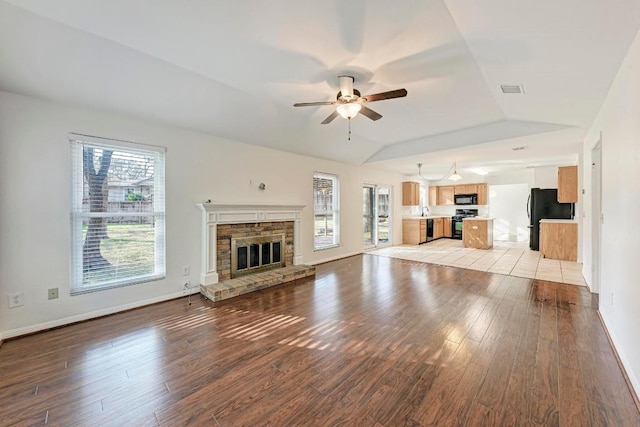 unfurnished living room featuring lofted ceiling, sink, ceiling fan, light hardwood / wood-style floors, and a brick fireplace