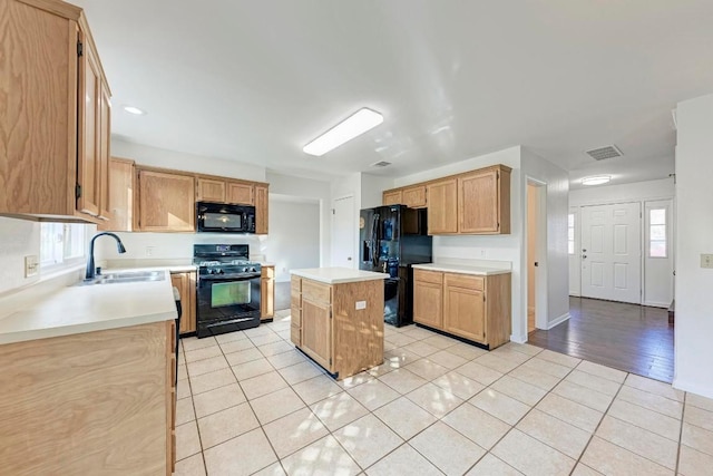 kitchen featuring light tile patterned flooring, light brown cabinetry, sink, a kitchen island, and black appliances