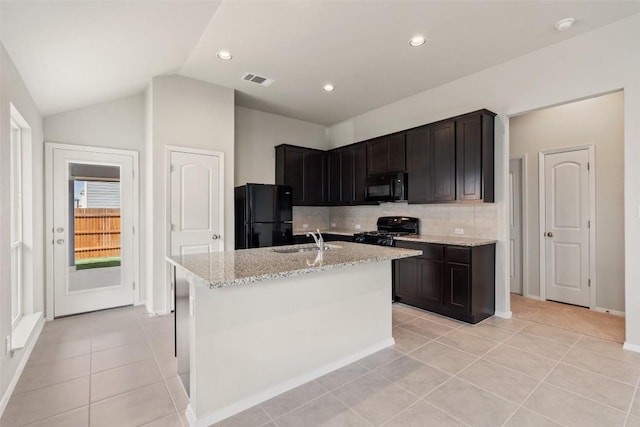 kitchen with light tile patterned flooring, sink, light stone counters, a kitchen island with sink, and black appliances