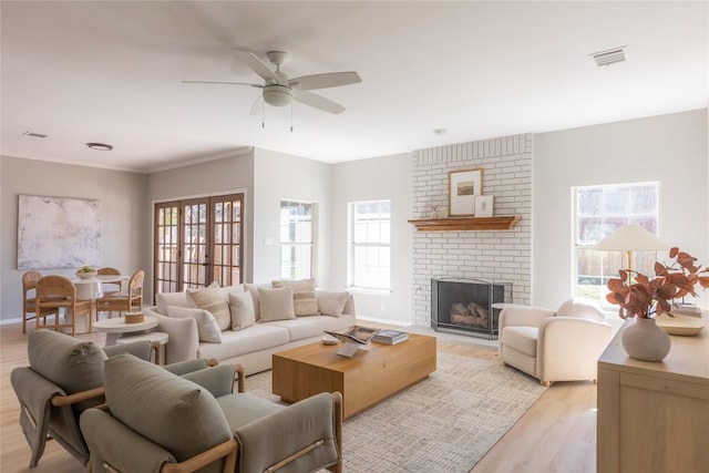 living room featuring a brick fireplace, a wealth of natural light, ceiling fan, and light hardwood / wood-style flooring