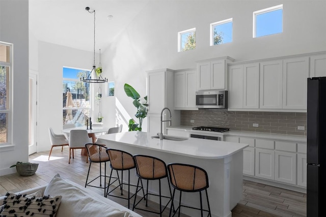 kitchen with decorative light fixtures, white cabinetry, sink, a kitchen island with sink, and black fridge