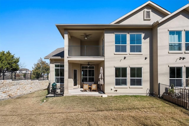 rear view of house with ceiling fan, a balcony, a patio, and a lawn