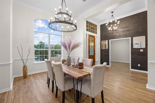 dining room with an inviting chandelier, wooden walls, a high ceiling, ornamental molding, and light wood-type flooring