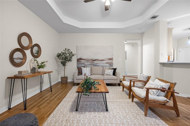 living room featuring light hardwood / wood-style flooring, a raised ceiling, and ceiling fan