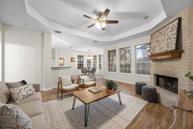 living room featuring ceiling fan, a fireplace, a raised ceiling, and light hardwood / wood-style flooring