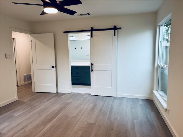 unfurnished bedroom featuring light hardwood / wood-style flooring, a barn door, and ensuite bathroom