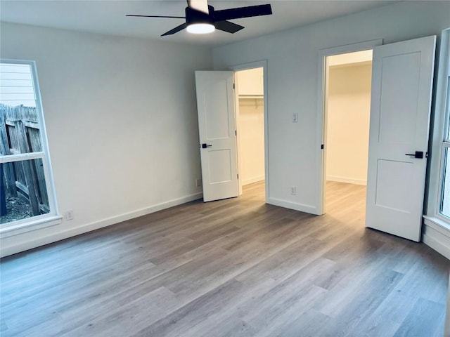 unfurnished bedroom featuring light hardwood / wood-style flooring, a walk in closet, a closet, and ceiling fan