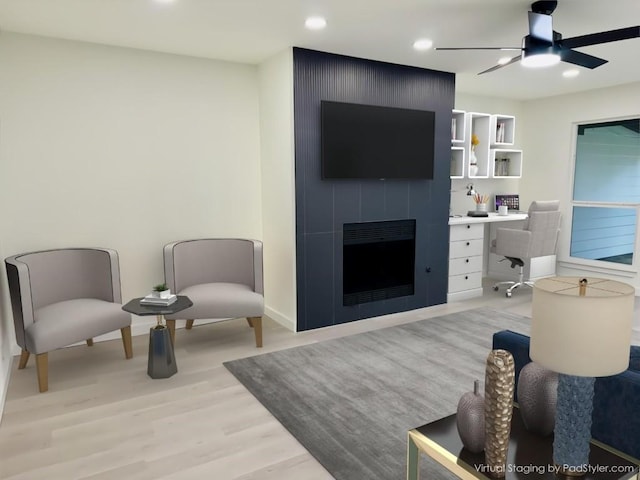 living room featuring a large fireplace, ceiling fan, and light wood-type flooring