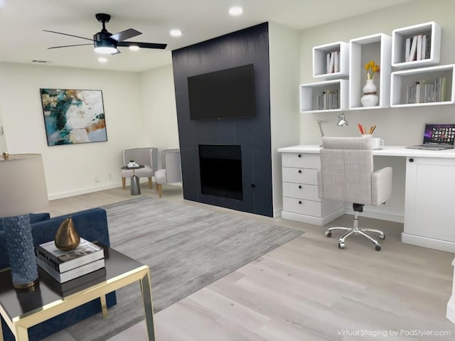 office with ceiling fan, a large fireplace, and light wood-type flooring