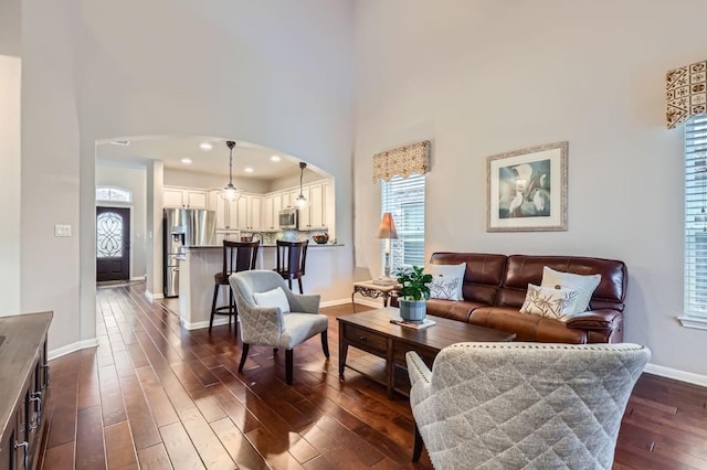 living area featuring arched walkways, recessed lighting, dark wood-type flooring, a towering ceiling, and baseboards