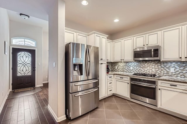 kitchen with baseboards, decorative backsplash, light stone counters, stainless steel appliances, and recessed lighting