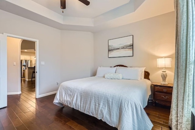 bedroom with arched walkways, dark wood finished floors, a raised ceiling, ceiling fan, and baseboards