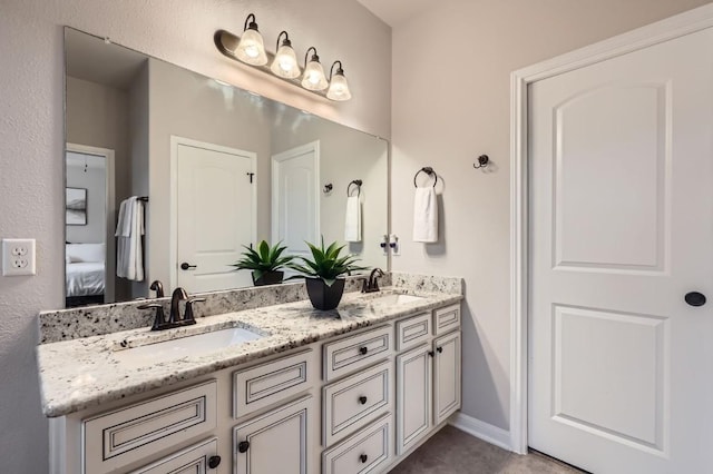 full bath with double vanity, ensuite bath, a sink, and baseboards