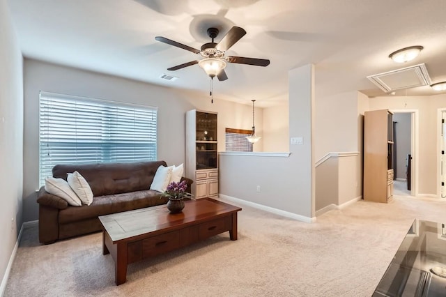 living area with light carpet, visible vents, a ceiling fan, baseboards, and attic access