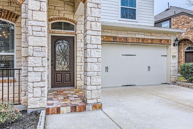 doorway to property featuring a garage, stone siding, and concrete driveway