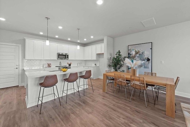 kitchen featuring white cabinetry, an island with sink, light hardwood / wood-style flooring, and pendant lighting