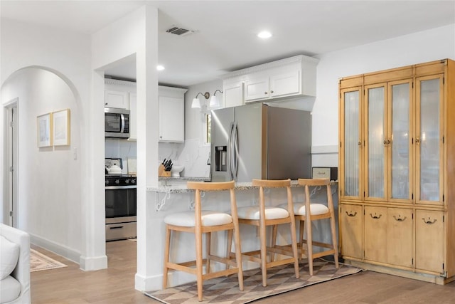 5410 Overbrook Dr, Austin, TX 78723 - kitchen featuring appliances with stainless steel finishes, light wood-style floors, a kitchen breakfast bar, recessed lighting, and white cabinets