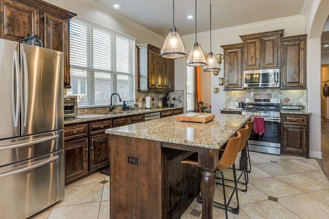 kitchen with hanging light fixtures, a center island, stainless steel appliances, light stone countertops, and dark brown cabinets