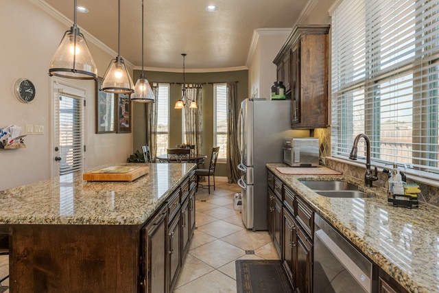 kitchen with a kitchen island, decorative light fixtures, sink, crown molding, and light stone countertops