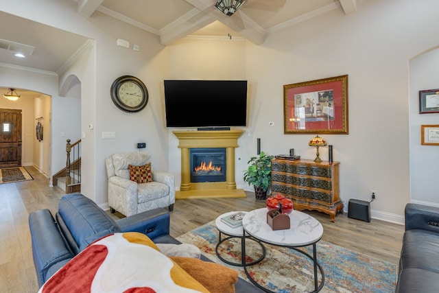 living room featuring beamed ceiling, ornamental molding, and light wood-type flooring