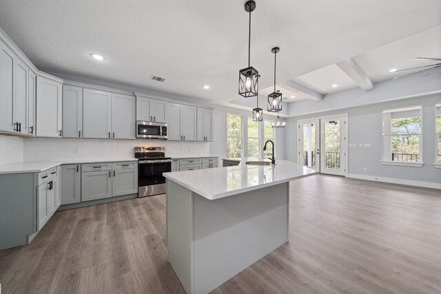 kitchen with gray cabinets, appliances with stainless steel finishes, pendant lighting, an island with sink, and sink